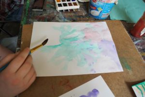 Hand mit Pinsel über einer Aquarellmalerei, Farbkasten